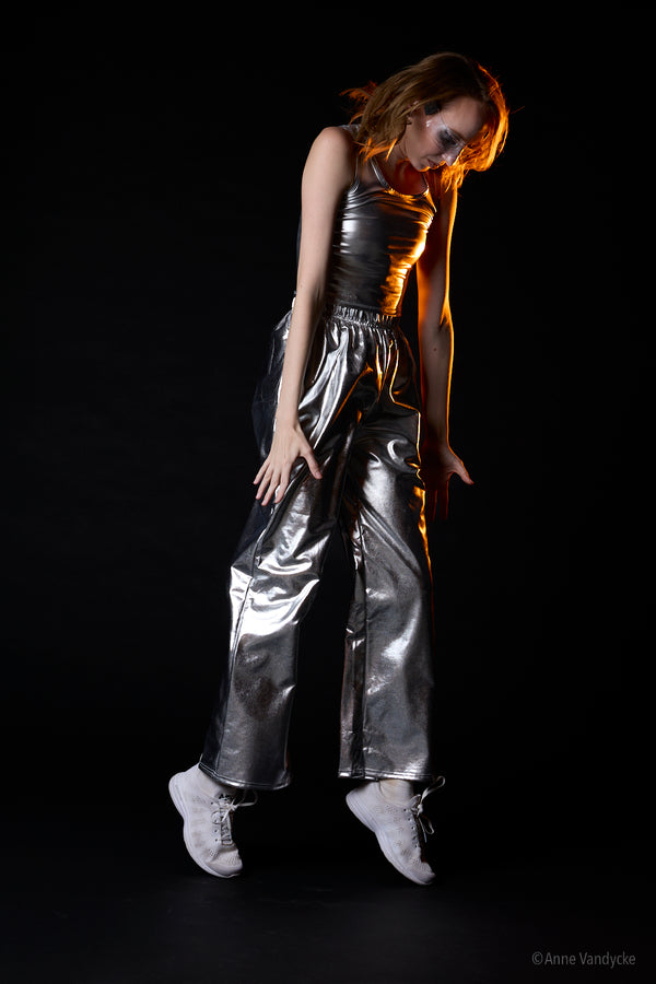 Person jumping, wearing a metallic outfit on a black background. Studio photo by Anne Vandycke, NY photographer.