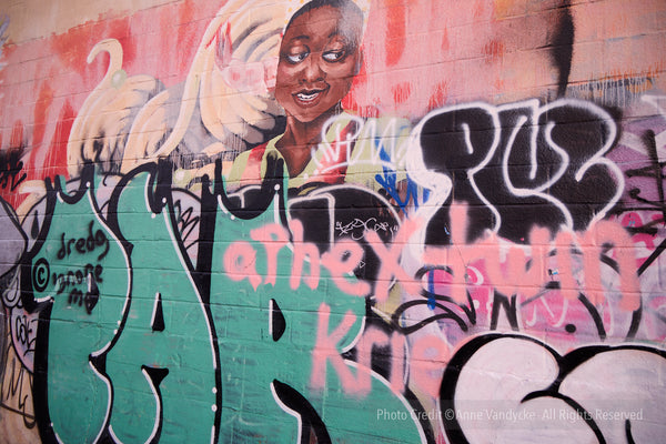 Graffiti art on a wall with colorful text and a stylized face. Photography by Anne Vandycke.