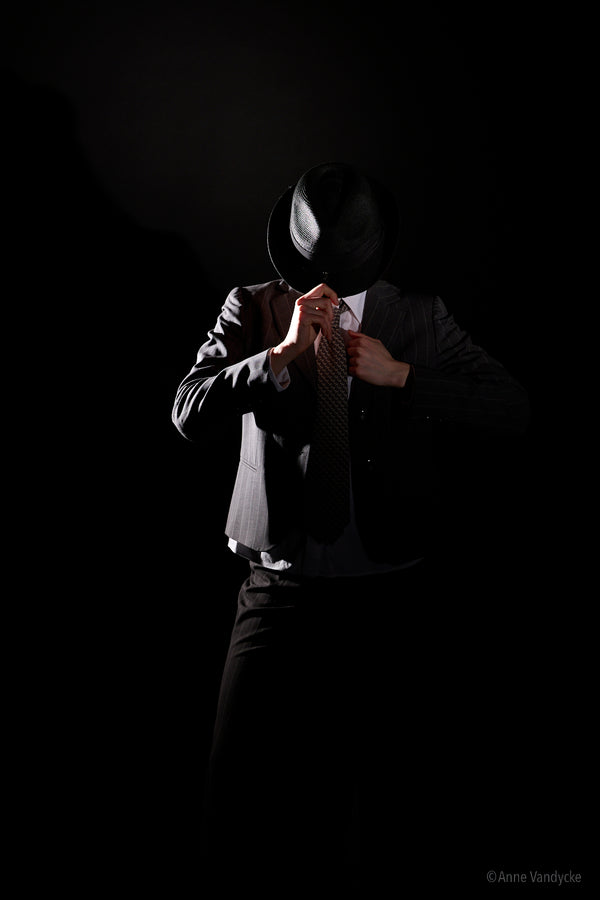 Person in a suit and hat against a dark background. Studio photography by New York photographer Anne Vandycke.