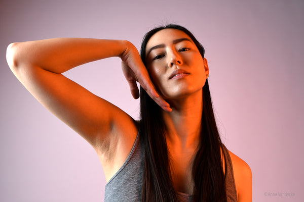 Woman posing with one hand on her face against a plain background. Skincare photo ad styled and shot by Anne Vandycke.