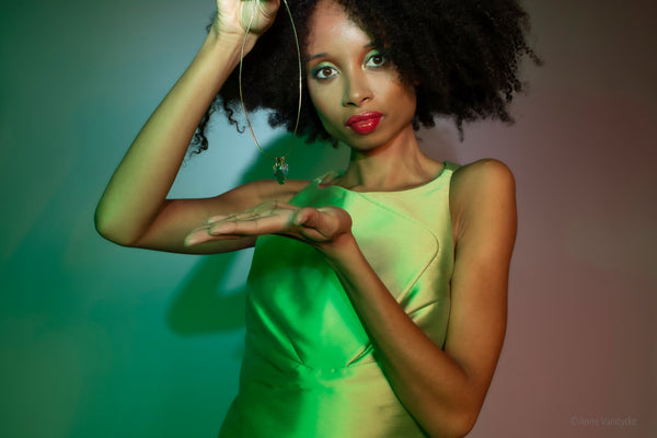 Model wearing green dress, showing off a necklace with large green pendent. Photo by Anne Vandycke.