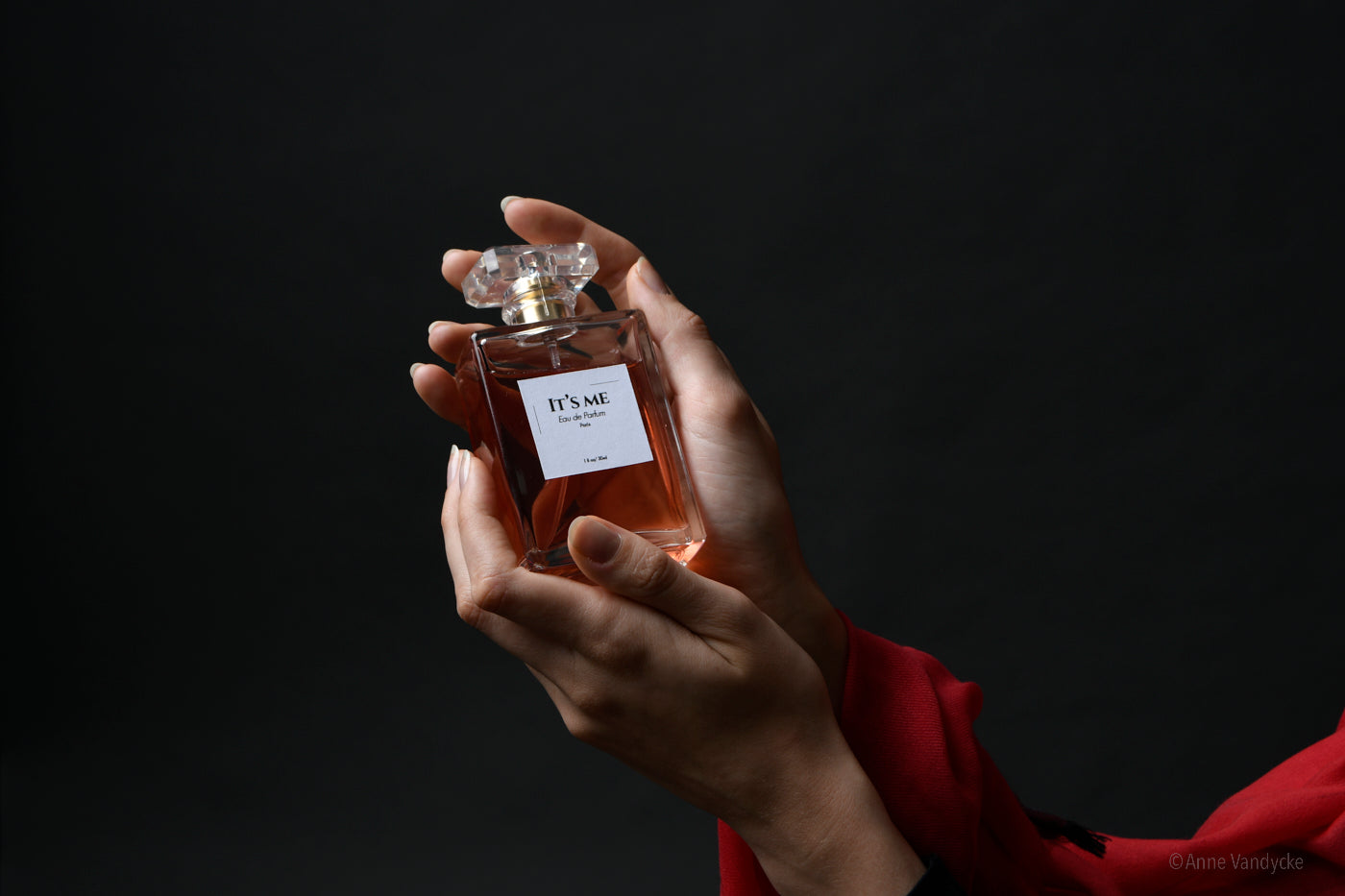 Hands holding a perfume bottle against a dark background. Photo ad by New York Photographer, Anne Vandycke.
