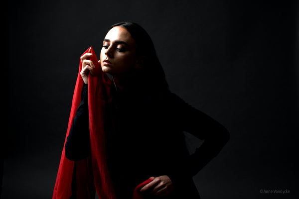 Woman holding a red fabric against a dark background. Photo style and shot by NY photographer, Anne Vandycke.