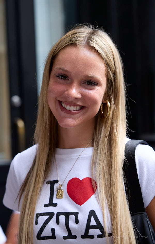 Woman wearing a white t-shirt with 'I ❤️ ZTA' design, smiling outdoors. Photo by New York Photographer, Anne Vandycke.
