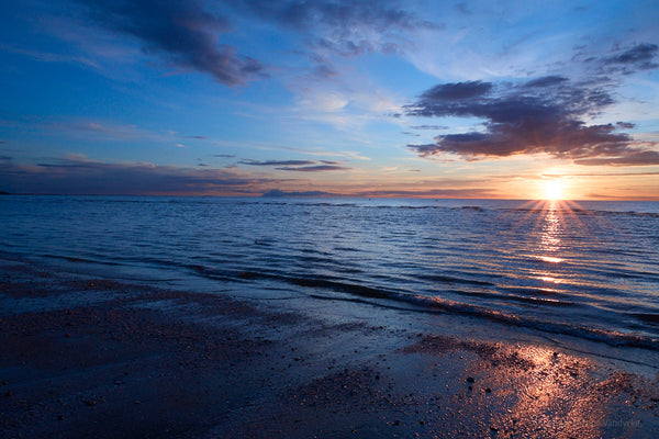 Sunset over a calm sea with a beach in the foreground. Photo taken by Anne Vandycke, NYC photographer.