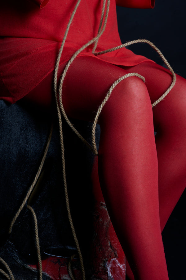 Person wearing red outfit, with dark background and rope.