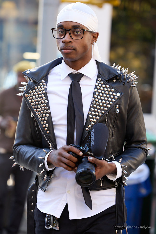 Man wearing a studded leather jacket and holding a camera. Photo by New York Photographer, Anne Vandycke.