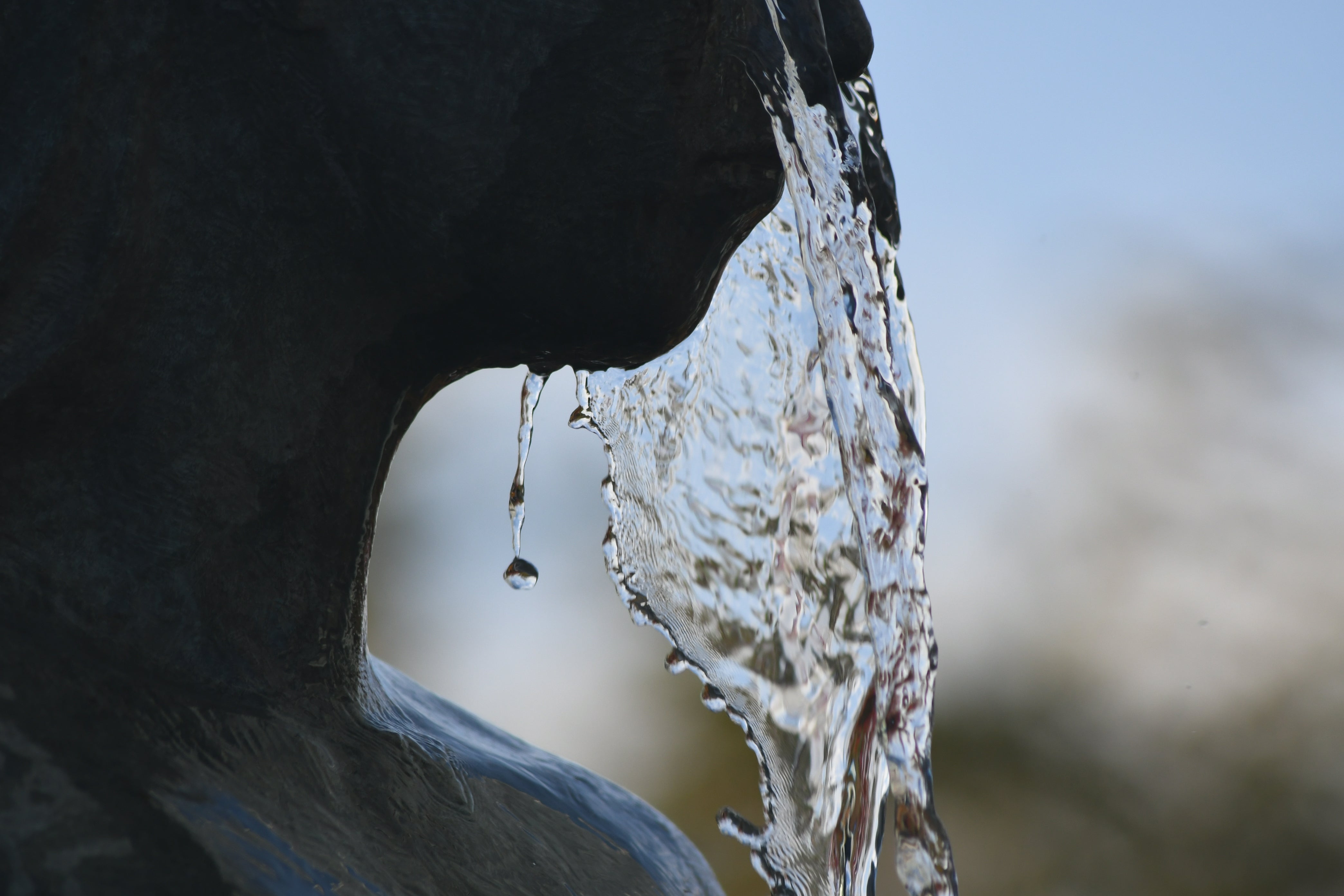 Close-up of water dripping from a stone surface with a blurred natural background. Architecture photography by Anne Vandycke.