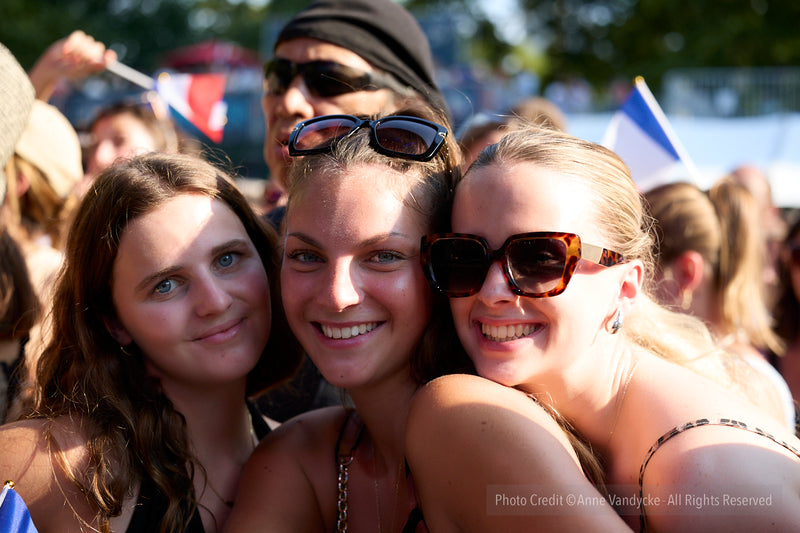 Three women posing together surrounded by a crowd at an outdoor event. Photo by New York photographer, Anne Vandycke.
