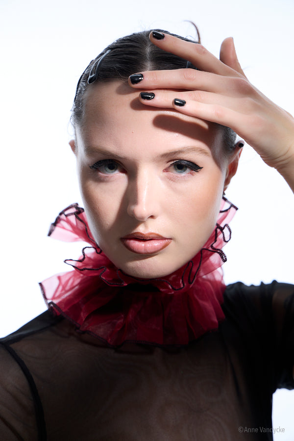 Woman with a red ruffled collar and black top against a white background. Picture captured by New York photographer, Anne Vandycke.