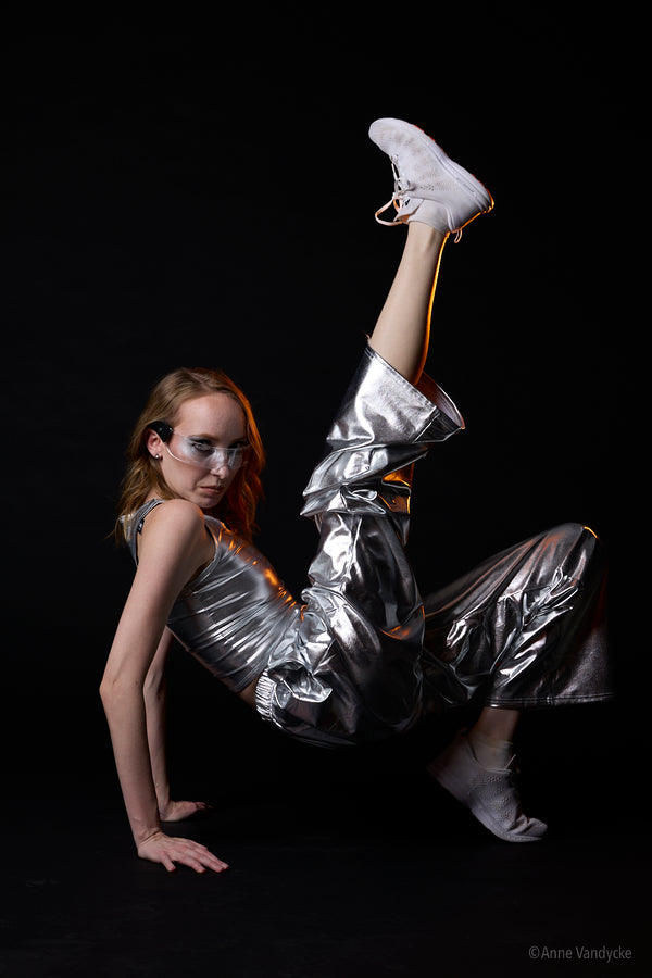 Woman wearing silver reflective outfit and white sneakers posing against a black background. Photo by New York photographer, Anne Vandycke.