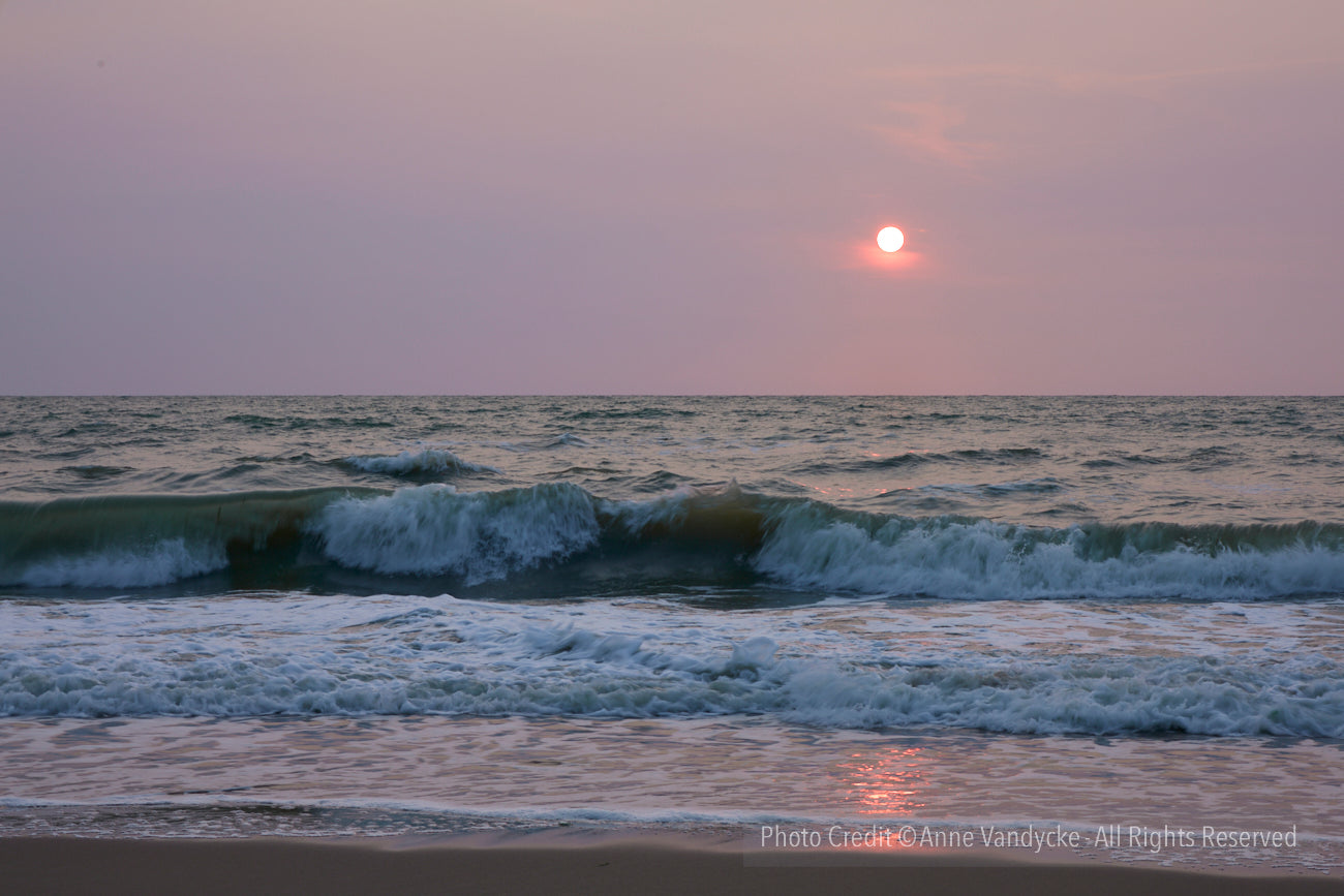 Sunset over the ocean with waves crashing on the shore. Sunset photo by New York artist, Anne Vandycke.