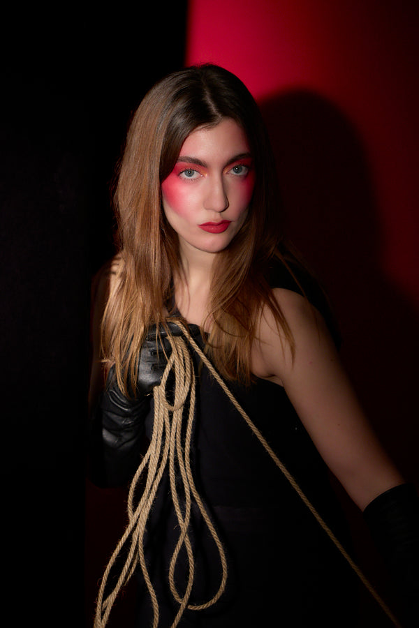 Woman holding a rope against a dark, red background. Photo by artist and photographer, Anne Vandycke.