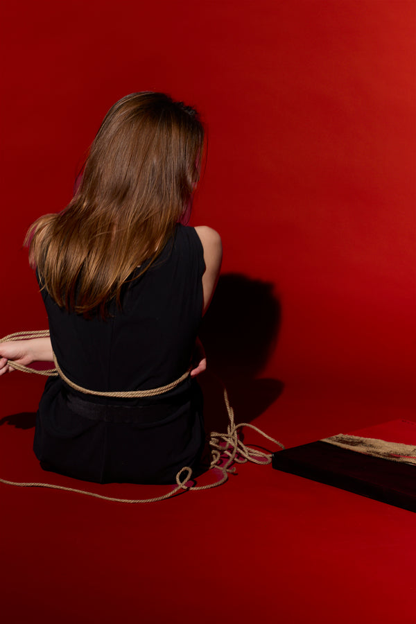 Photo by New York photographer, Anne Vandycke. Woman sitting on the ground with back to camera with a red background.