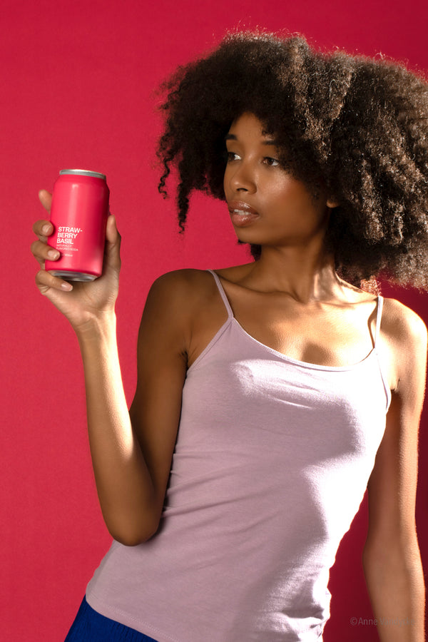 Woman holding a pink soda can against a matching pink background. Photo by NY photographer, Anne Vandycke.