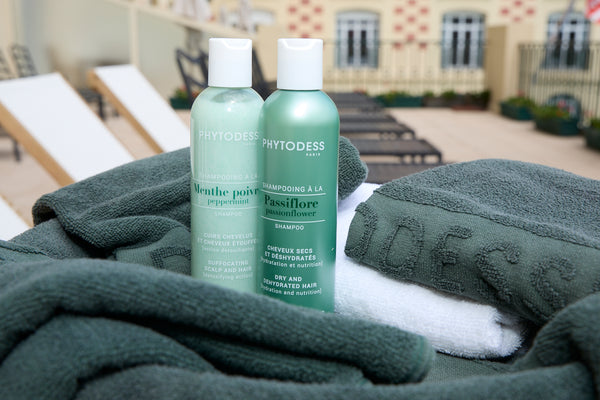 Two bottles of Phytodess shampoo on a towel with a blurred outdoor background. Styled photography by Anne Vandycke.