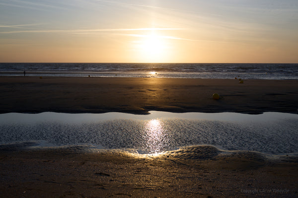 Sunset over a beach with a person walking on the sand. Photograph by Anne Vandycke.