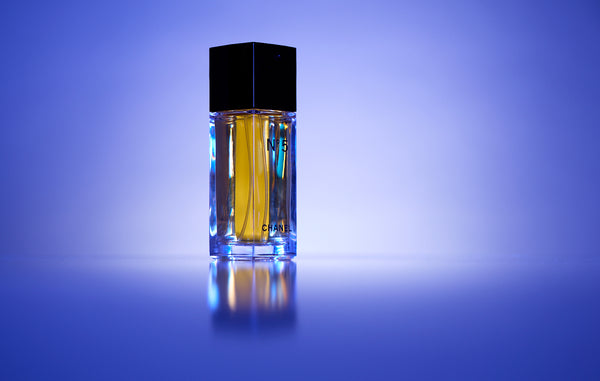 Small glass bottle of Chanel perfume with a black cap on a reflective purple surface. Photography by Anne Vandycke, New York Photographer.