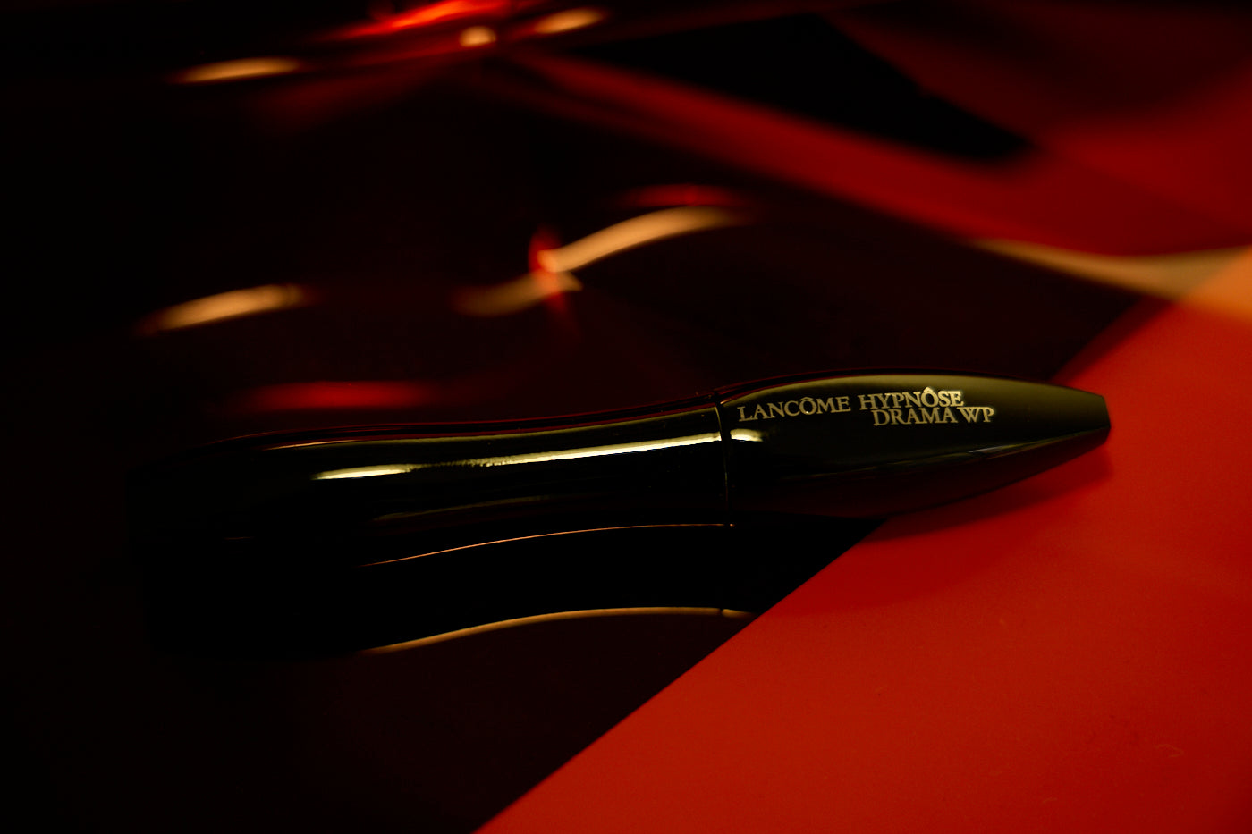 Lancème mascara on a dark surface with red background. Photo styled and shot by New York photographer, Anne Vandycke.