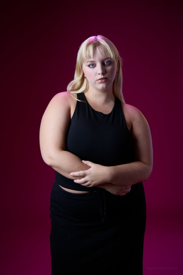 Woman wearing a black sleeveless top and skirt against a purple background. Studio Photoshoot by New York Photographer, Anne Vandycke.